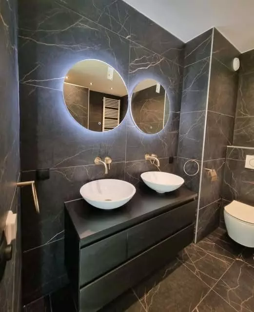 Badkamer renovatie in Kampen met donkergrijze marmerlook tegels, messing kranen en LED spiegels