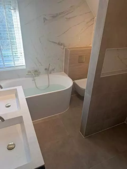 Badkamer renovatie in Ootmarsum met lichte warme tinten, marmerlook tegels en ligbad met nis